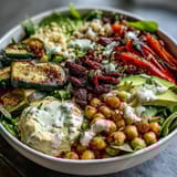 Hearty Vegan Mediterranean Buddha Bowl topped with creamy hummus, kalamata olives, and colorful roasted vegetables, ready to serve.