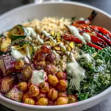 Close-up of a colorful Mediterranean Buddha Bowl Meal Prep, featuring bulgur pilaf with pistachios, roasted eggplant, steamed kale, and creamy tahini dressing.  