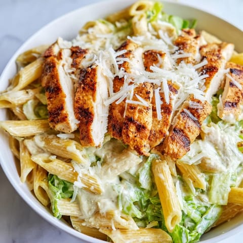 Bright forkfuls of Spicy Chicken Caesar Pasta with cherry tomatoes, parmesan, and croutons on a rustic table.