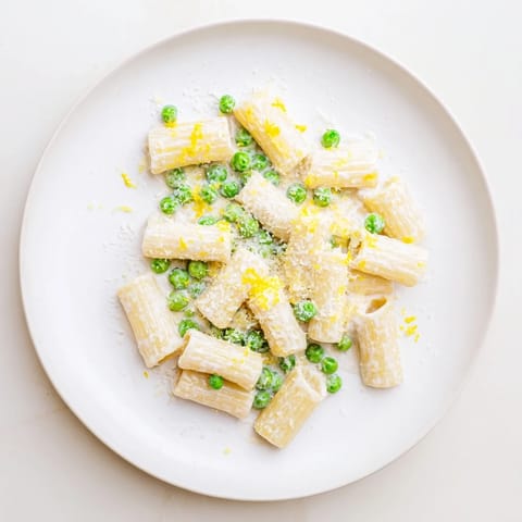 Bright green peas and creamy ricotta sauce cling to perfectly cooked rigatoni in this vibrant Pea & Lemon Ricotta Pasta, garnished with fresh basil.  
