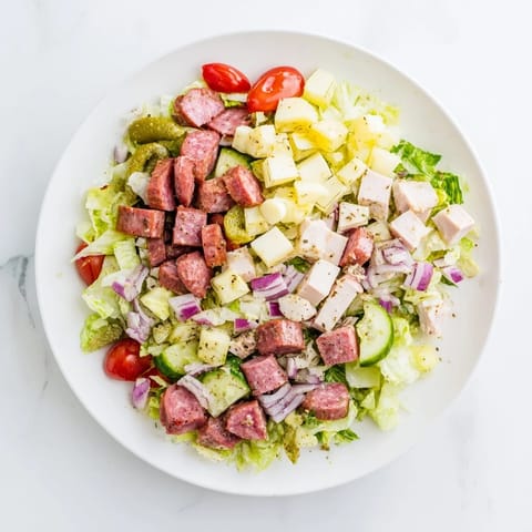 Hearty Italian Deli Chopped Chicken Salad tossed with a tangy herb dressing, featuring juicy chicken, salty salami, and crunchy vegetables on a rustic wooden table.
