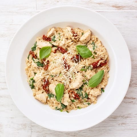 Golden-brown Tuscan Chicken Orzo simmering in a creamy, garlicky sauce with sun-dried tomatoes and spinach.