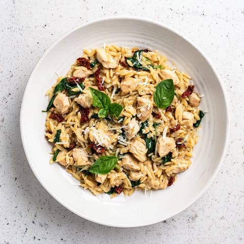 Fresh basil garnishes a hearty skillet of Tuscan Chicken Orzo, perfect for a comforting weeknight dinner.