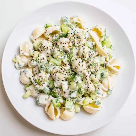 Chilled Cucumber Crunch Pasta Salad served in a white bowl, green onions and fresh dill sprinkled over the creamy, sesame-speckled pasta.  