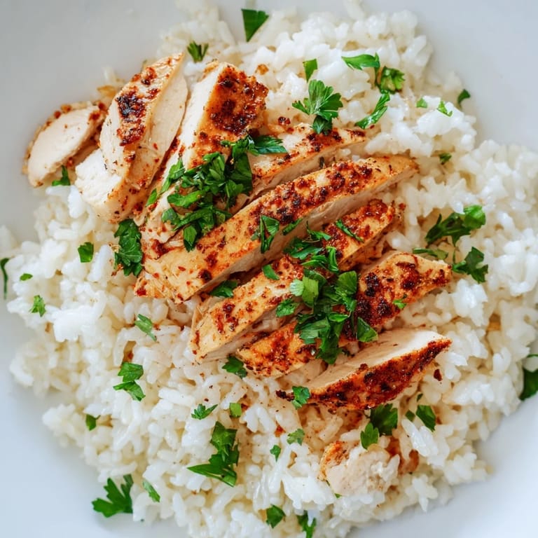 A fork gently lifts a bite of Garlic Butter Rice with Chicken, revealing golden, buttery grains studded with minced garlic and savory grilled chicken pieces.