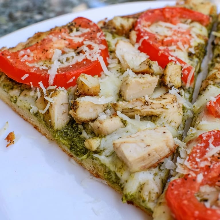 Freshly baked Chicken Pesto Pizza topped with juicy tomatoes and basil leaves, ready to slice and serve.