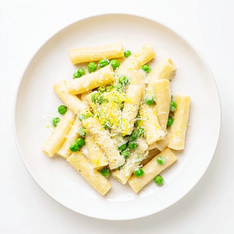 A close-up of steaming Pea & Lemon Ricotta Pasta shows zesty lemon zest and grated Parmesan sprinkled over the cheesy, spring-green sauce.  