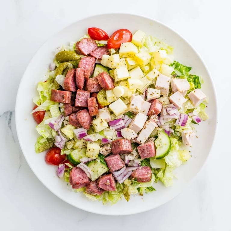 Hearty Italian Deli Chopped Chicken Salad tossed with a tangy herb dressing, featuring juicy chicken, salty salami, and crunchy vegetables on a rustic wooden table.